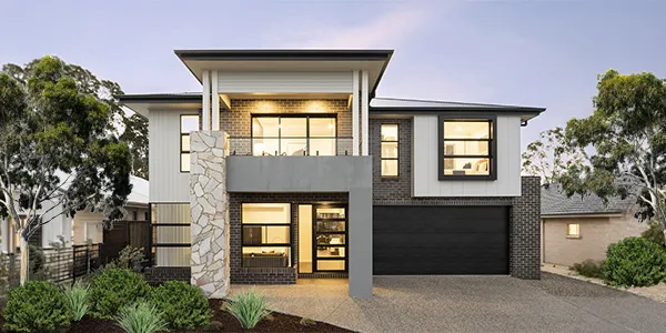 Modern two-story display home with white and dark gray exterior, featuring large windows, brick and rendered facade accents, black garage door, and landscaped front garden with native plants and trees at dusk.