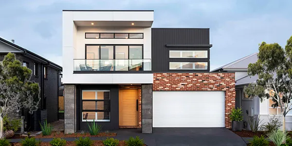 Modern two-story residential home with mixed facade materials including white render, dark charcoal cladding, and red brick. Features large multi-pane windows on upper level, horizontal wood-grain entry door, white garage door, and landscaped front garden with native plants and trees. Located in Box Hill.