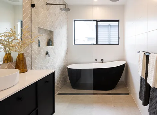 Modern luxury bathroom featuring a freestanding black oval bathtub, white vessel sink with black vanity, herringbone tile shower enclosure, and contemporary window with black frame.