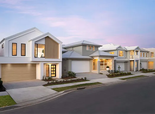 Row of modern residential homes at dusk in Oran Park, featuring contemporary architecture with white and grey facades, illuminated windows, garage doors, manicured lawns, and a quiet street.