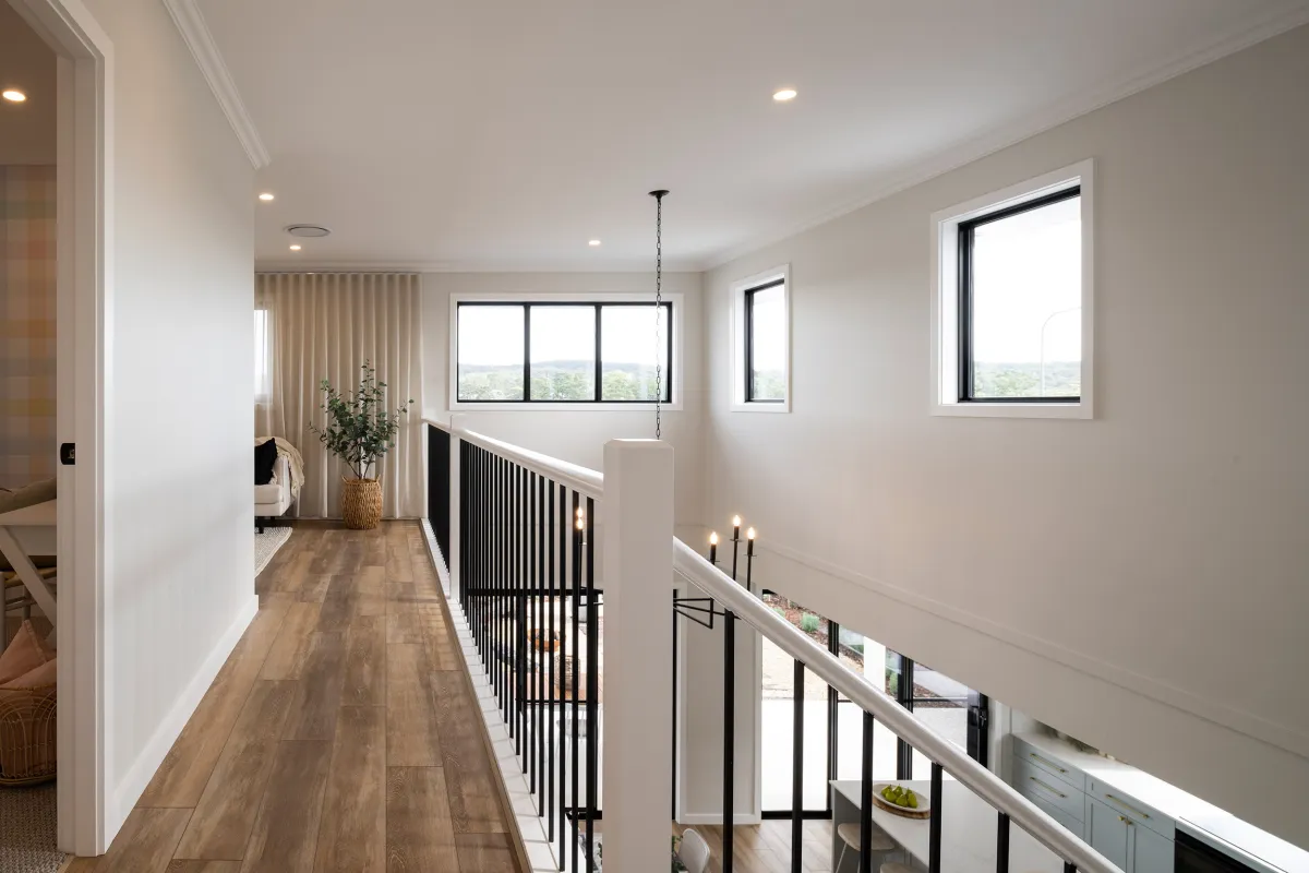 Montgomery Homes Waverley 324 display home upper void featuring a bright hallway with wooden flooring, white walls, black metal railings, multiple windows with landscape views, recessed lighting, and a pendant light fixture overhead.