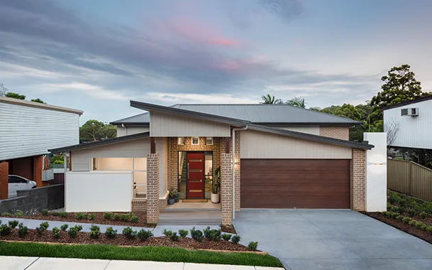 Modern single-story brick and white rendered house with dark roof, red front door, and brown garage door set in Illawarra landscape with mature trees and neighboring homes visible.
