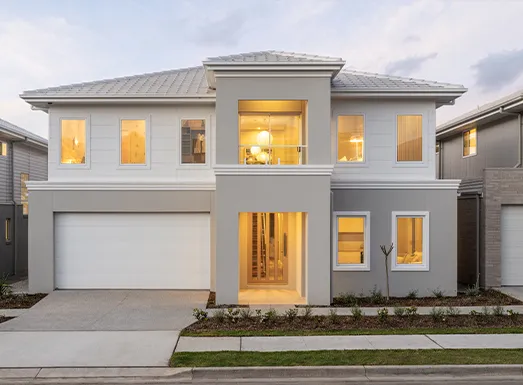 Modern two-story gray and white house with illuminated windows, white garage door, metal roof, concrete driveway, and landscaping in front during dusk in a Sydney residential area.