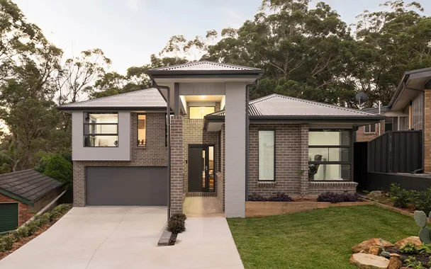 Modern two-story brick house with contemporary design, featuring a dark gray garage, large windows, white trim, metal roof, and manicured front lawn surrounded by mature trees.