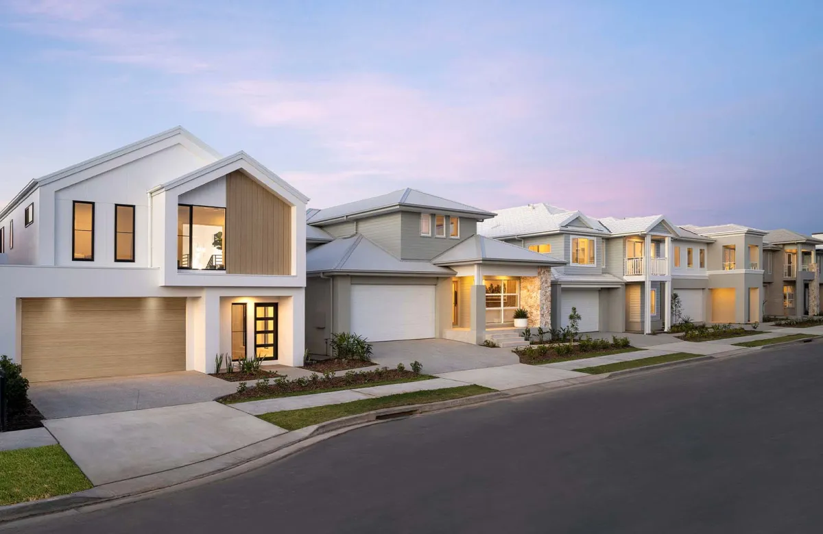 Montgomery Homes display homes in Oran Park, featuring a row of modern residential houses with contemporary architecture, illuminated windows, manicured lawns, and driveways along a suburban street at dusk.