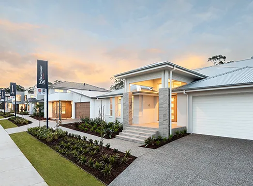 Modern single-story residential home with white and gray exterior, illuminated interior, metal roof, double garage, manicured front lawn, and landscaping at dusk with 