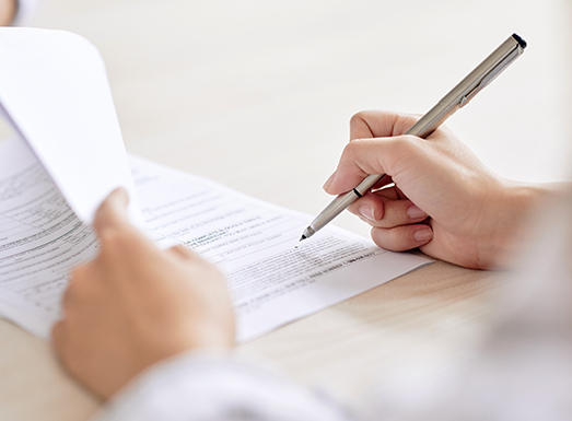 Person signing a contract document with a pen, holding the paperwork with one hand while writing with the other.