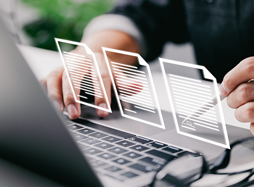 Person holding hands over laptop keyboard with three translucent document icons floating above the screen, representing digital file approvals and document management workflow.