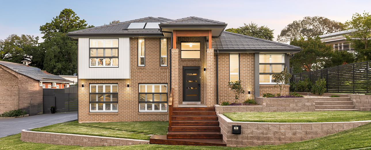 Modern brick house in Campbelltown with rendered and timber facade, featuring solar panels on roof, wooden front steps, large windows with shutters, manicured lawn with retaining walls, and neighboring properties visible on either side.