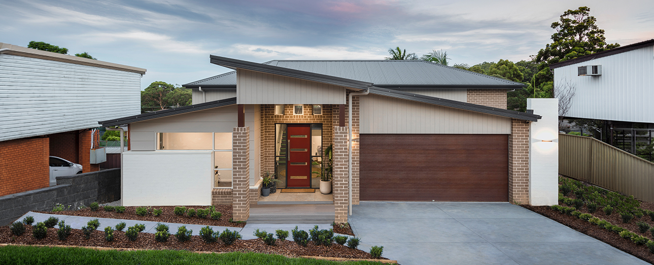 Modern single-story home in Engadine with brick and white rendered facade, dark metal roof, red front door, brown garage door, concrete driveway, and landscaped front garden with shrubs and mulch.