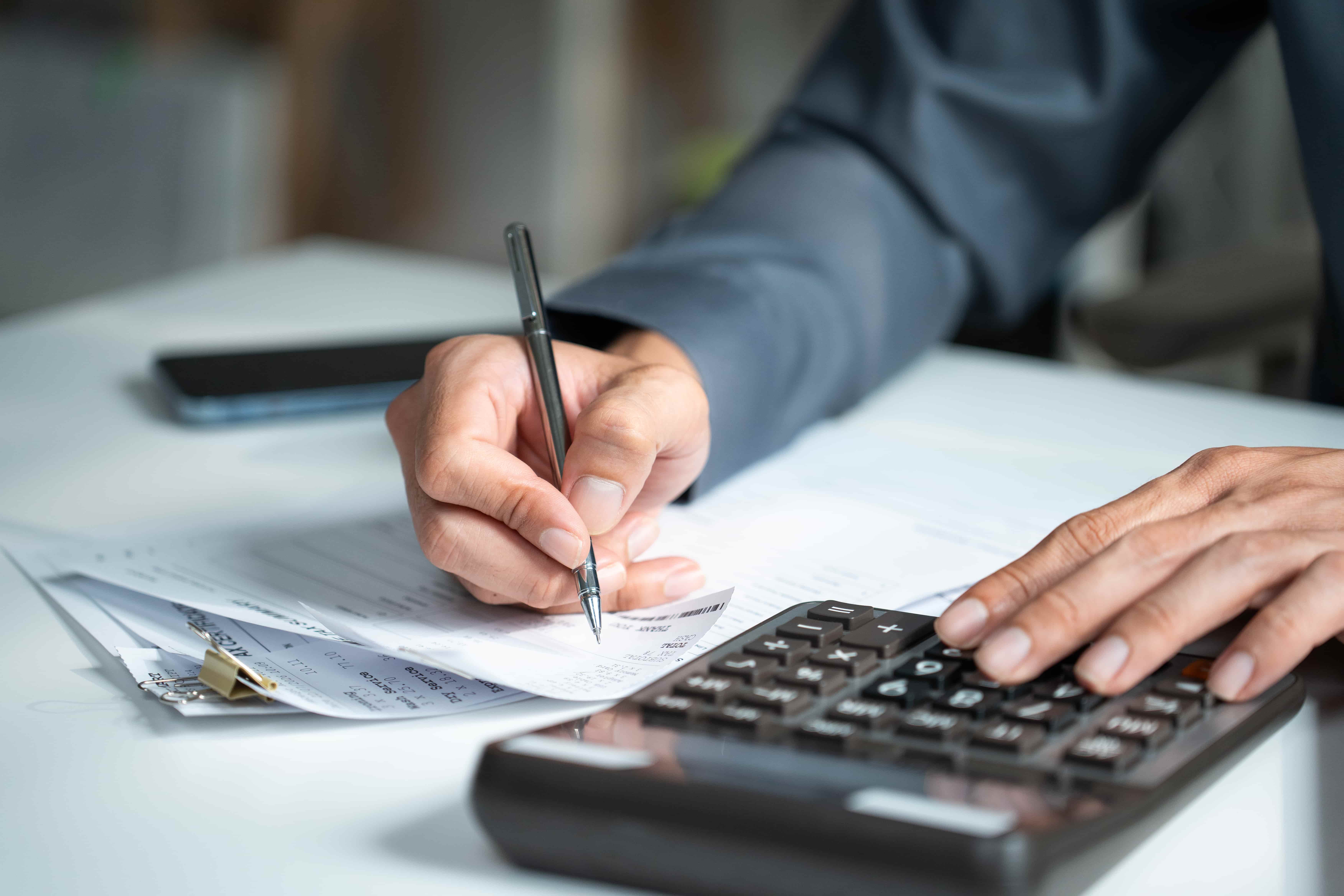Person in blue shirt signing a document with a pen while using a calculator, representing the deposit payment step in a house and land purchase process.