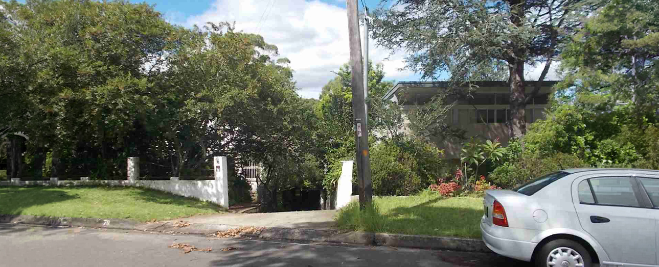 Killara residential property before renovation showing overgrown vegetation, white concrete fence, weathered house structure partially obscured by dense trees, and parked white sedan on street.